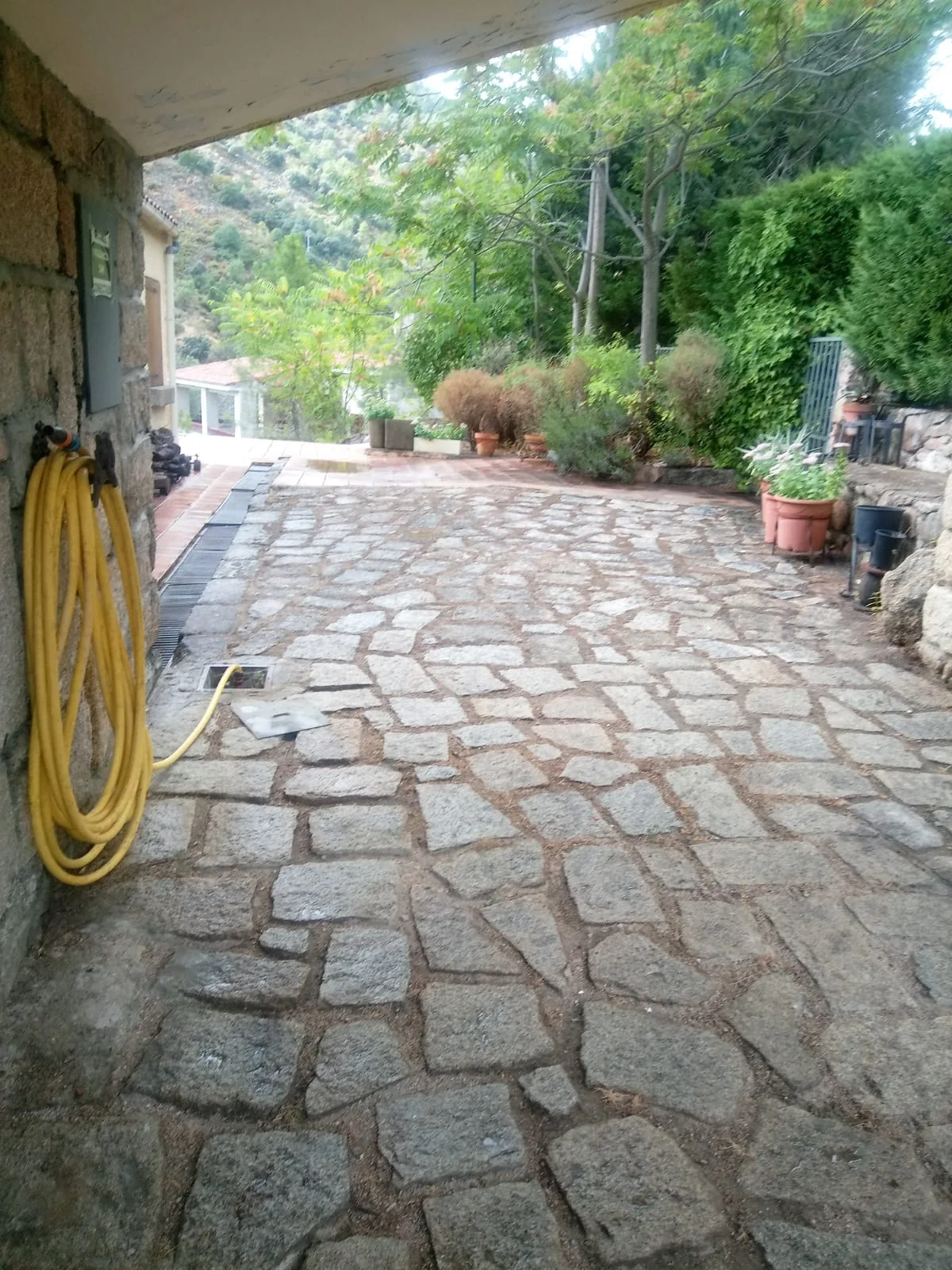 Camino de piedra junto al porche, con la manguera de riego recogida